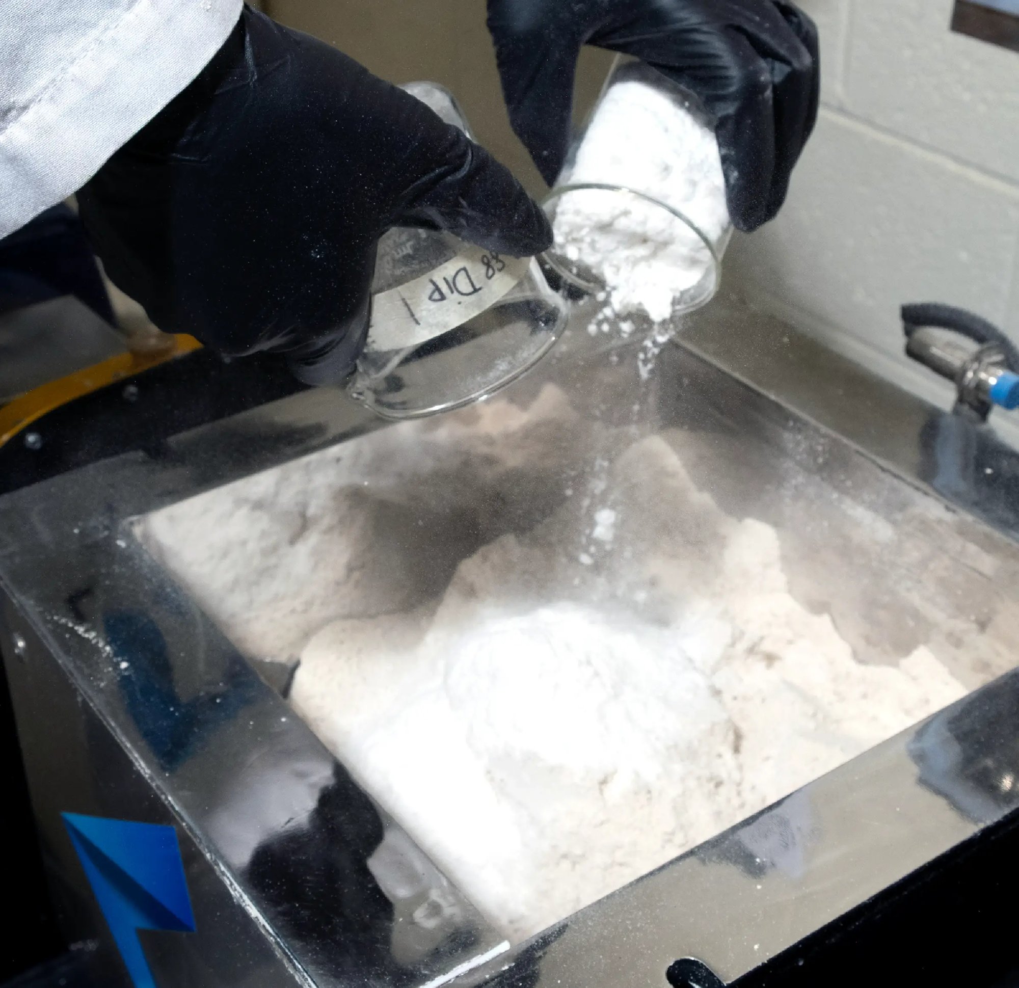 Technician adding powdered material to a mixing vessel during catalyst preparation and development at ActiveSite.