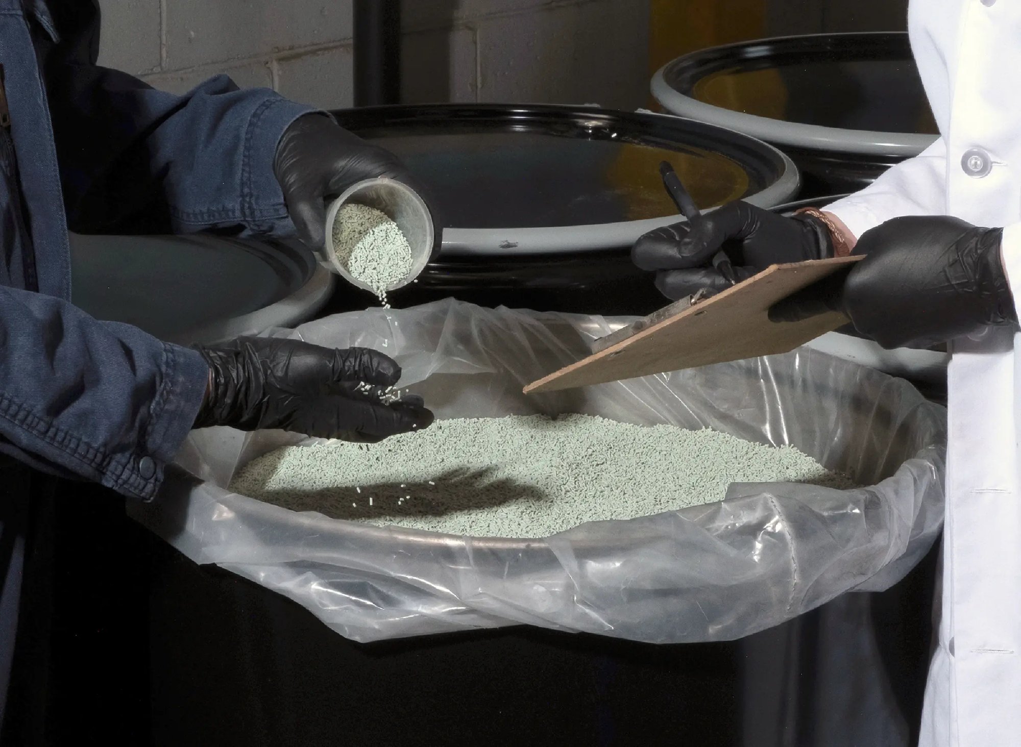 Technicians handling and sampling fine catalyst powder during a controlled materials processing operation.
