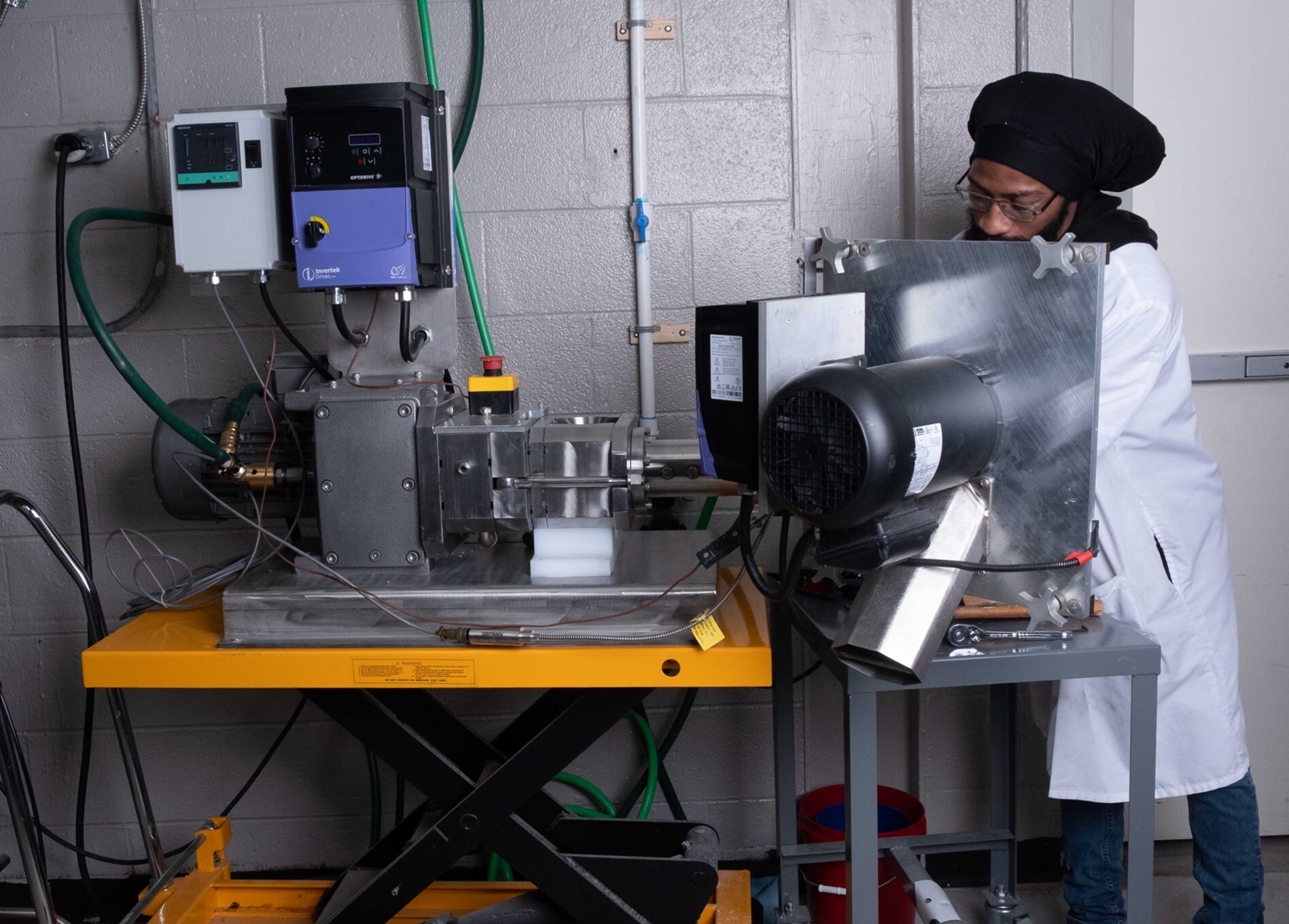 Technician operating a lab-scale catalyst extruder with variable-speed drive controls during a scale-up trial. Technician operating a lab-scale catalyst extruder with variable-speed drive controls during a scale-up trial.
