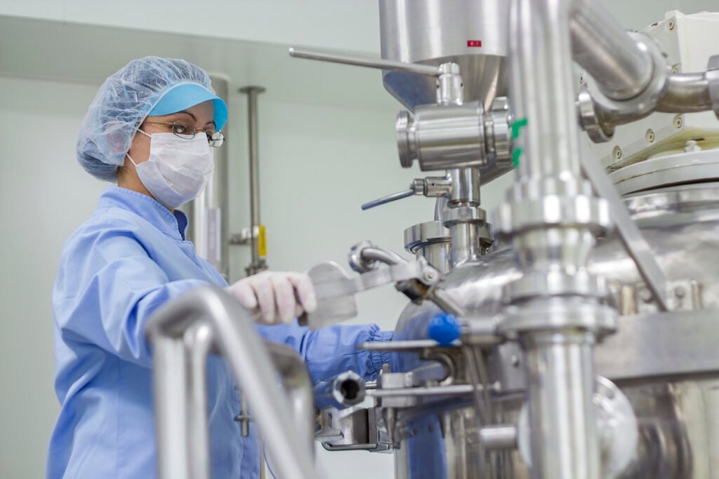 Preparing machine for work in pharmaceutical factory. Female worker wearing protective clothing in pharmaceutical plant.