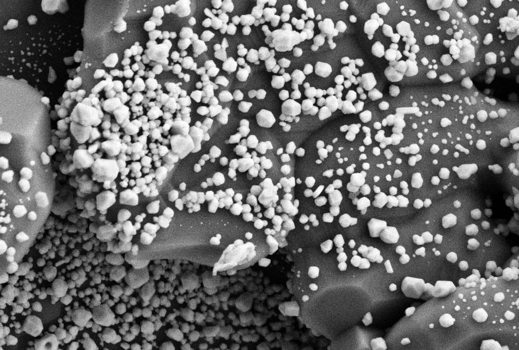 Scanning electron microscope (SEM) image showing clusters of nanoscale particles distributed across a textured catalyst surface at 20,000x magnification.