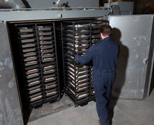 ActiveSite technician loading trays of catalyst material into an industrial drying oven for toll manufacturing.