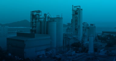Industrial manufacturing facility with processing towers and storage silos, shown with a blue overlay to represent advanced industrial technology and innovation.
