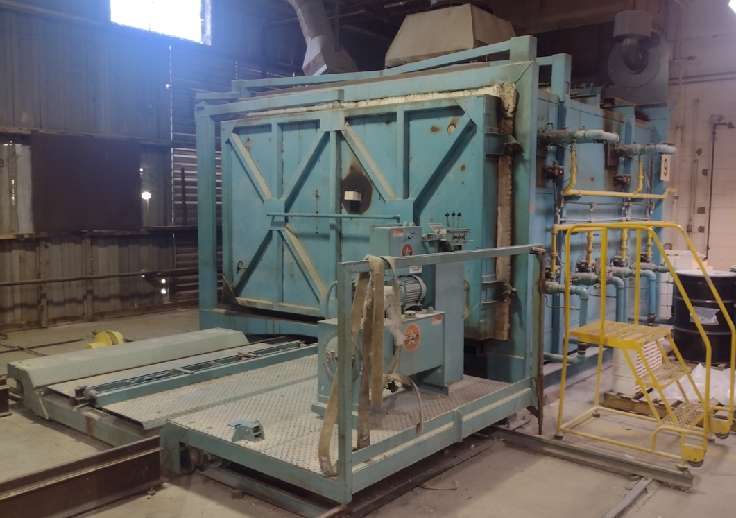 Industrial material toll manufacturing equipment inside a processing facility, featuring a large industrial processing unit, conveyor system, and connected piping.