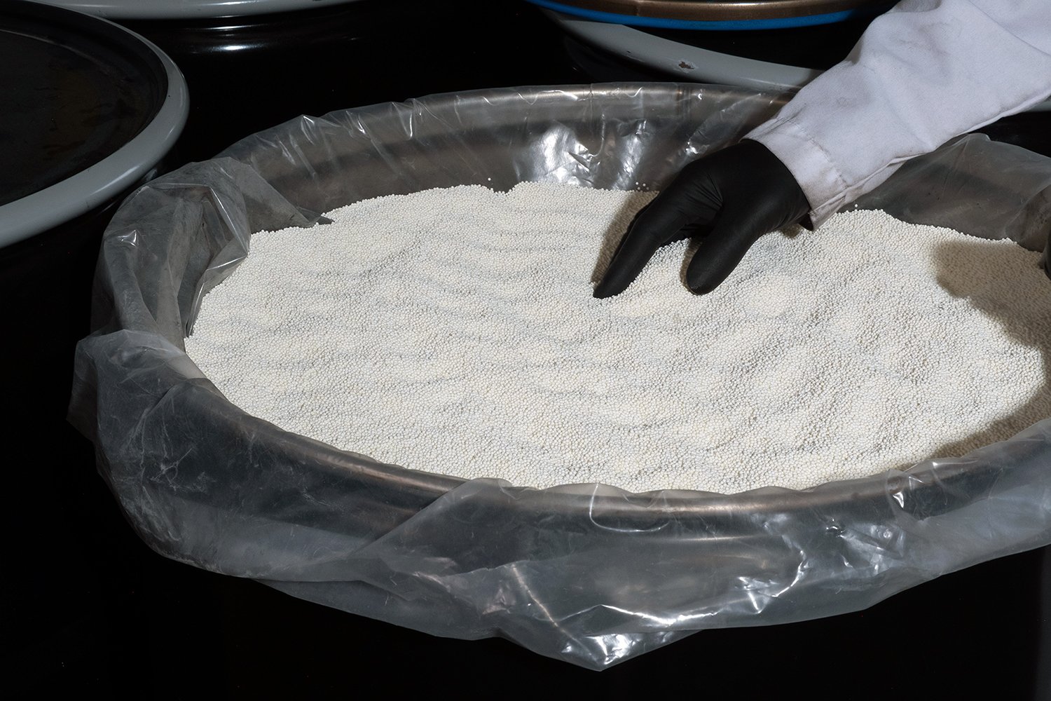 Gloved technician inspecting fine white material during a toll manufacturing process.